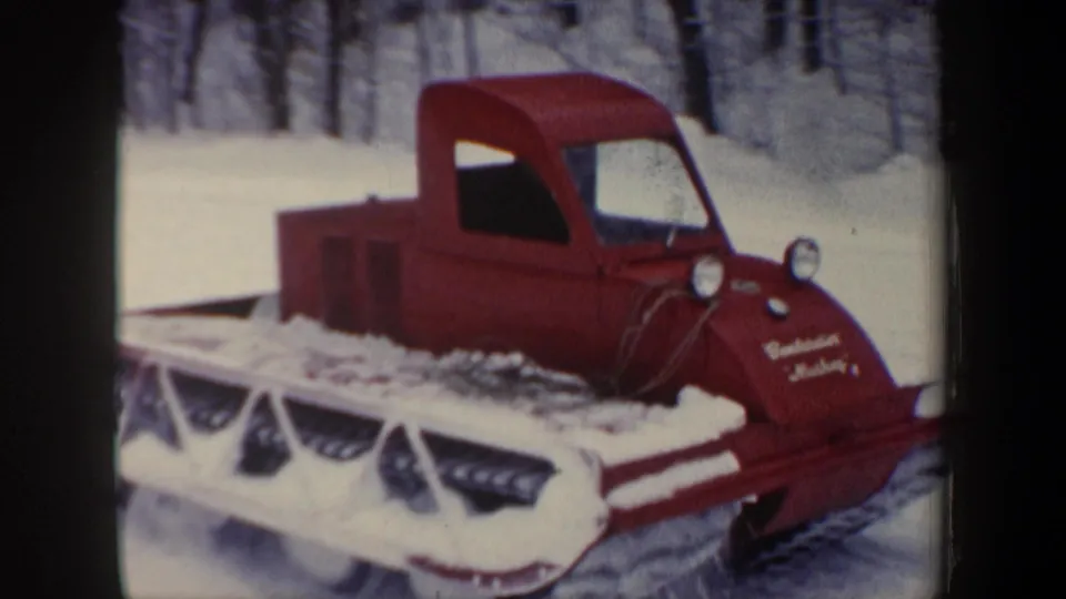 1962 New Hampshire home-movie frame with a red tracked snow vehicle and partial lettering on its nose in deep snow.