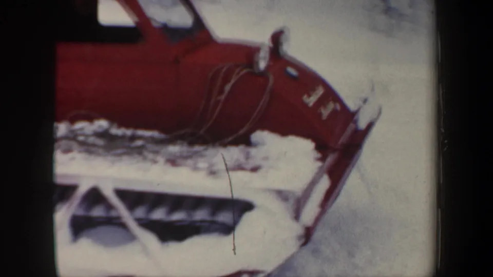 Close 8mm view of the red tracked snow vehicle in New Hampshire, with cab, hood, and snow-covered undercarriage visible.