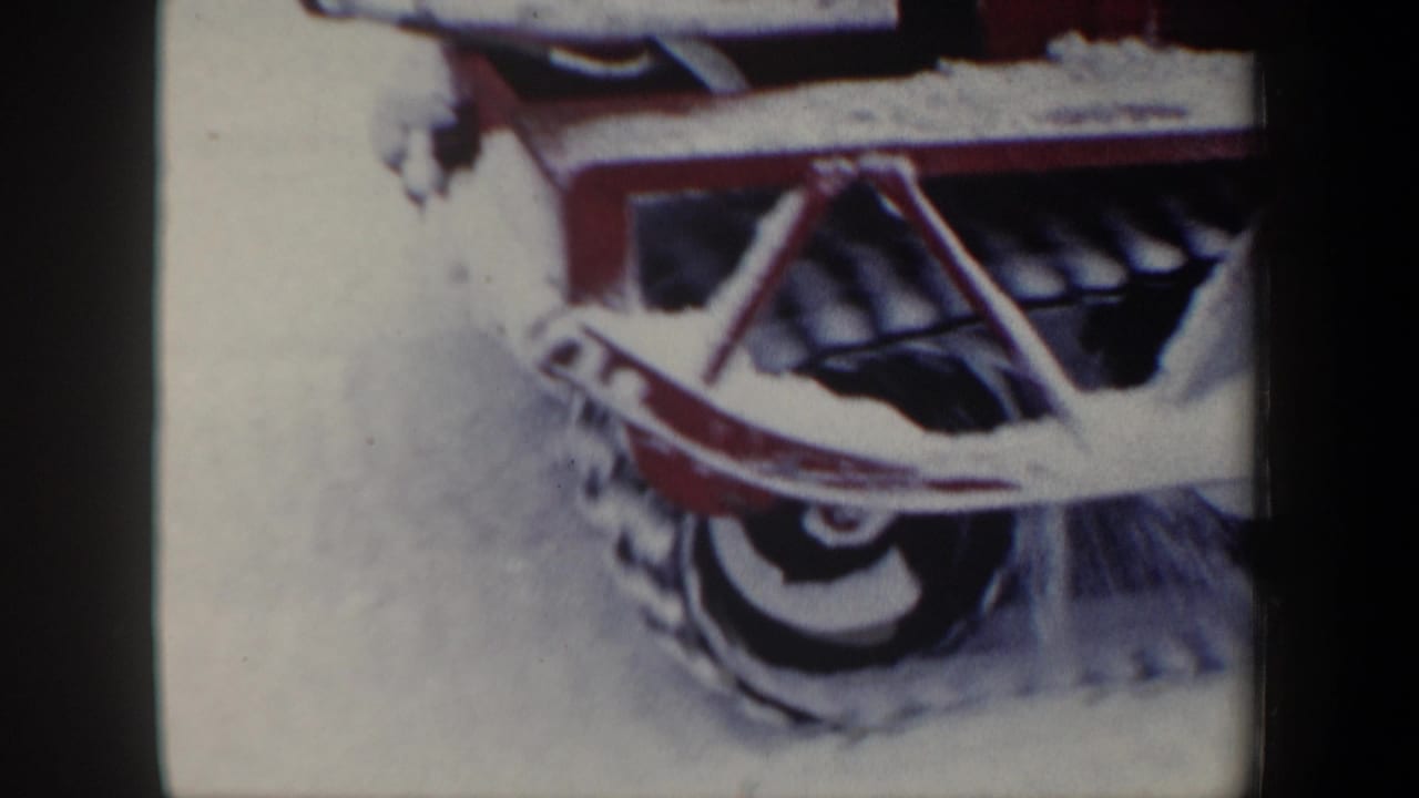 1962 New Hampshire 8mm frame showing the front blade and track of a red snowplow working through heavy snow.