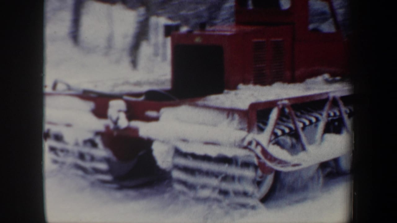 A red tracked snowplow faces the camera in a snowy New Hampshire landscape, with its blade and tracks visible.