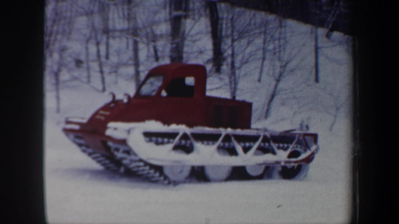 1962 New Hampshire 8mm frame showing a red tracked snow vehicle passing through snowy trees.