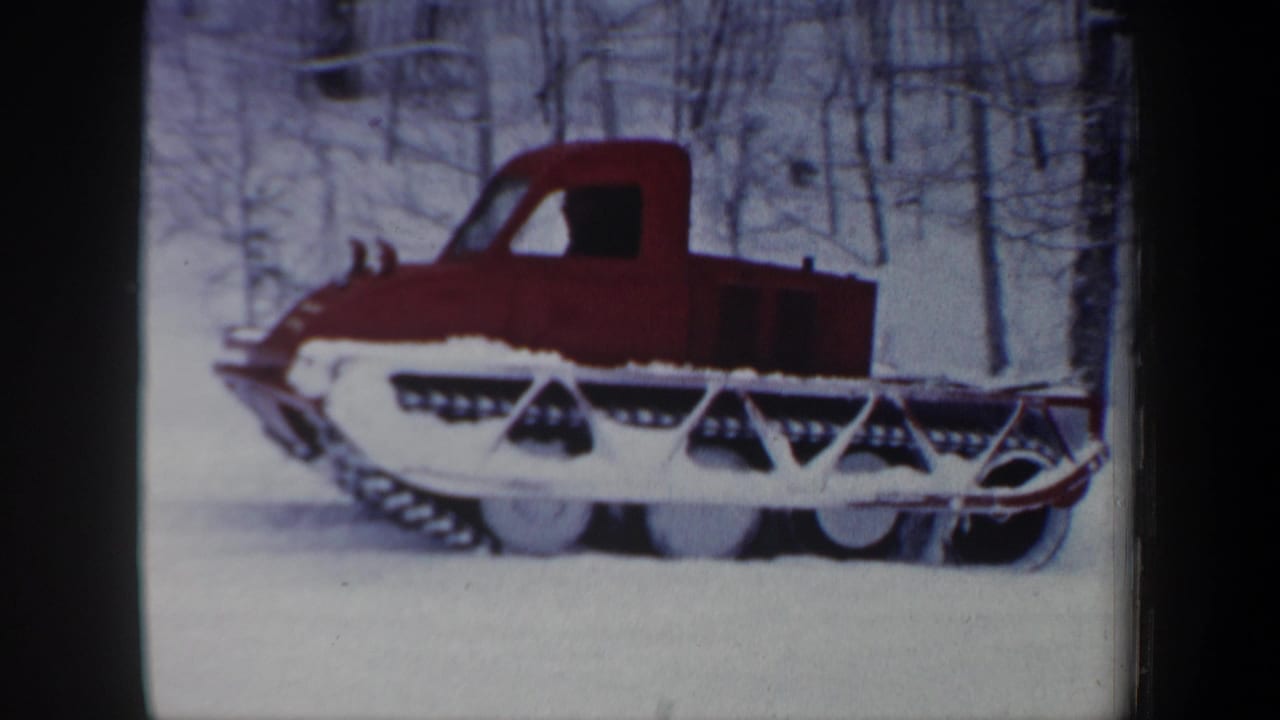 Red tracked snow vehicle in a winter New Hampshire forest, seen in a soft 8mm home-movie frame.
