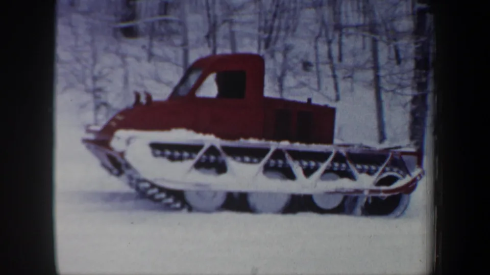 Red tracked snow vehicle in a winter New Hampshire forest, seen in a soft 8mm home-movie frame.