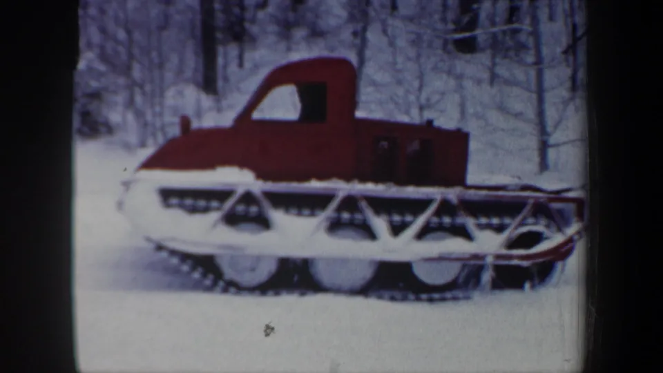 Close side view of the red tracked snow vehicle continuing through a snowy wooded setting in New Hampshire.