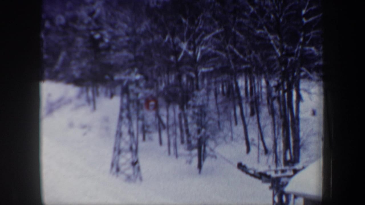 1962 New Hampshire home-movie frame showing a snow-covered forested slope with part of a ski lift visible near the lower right.