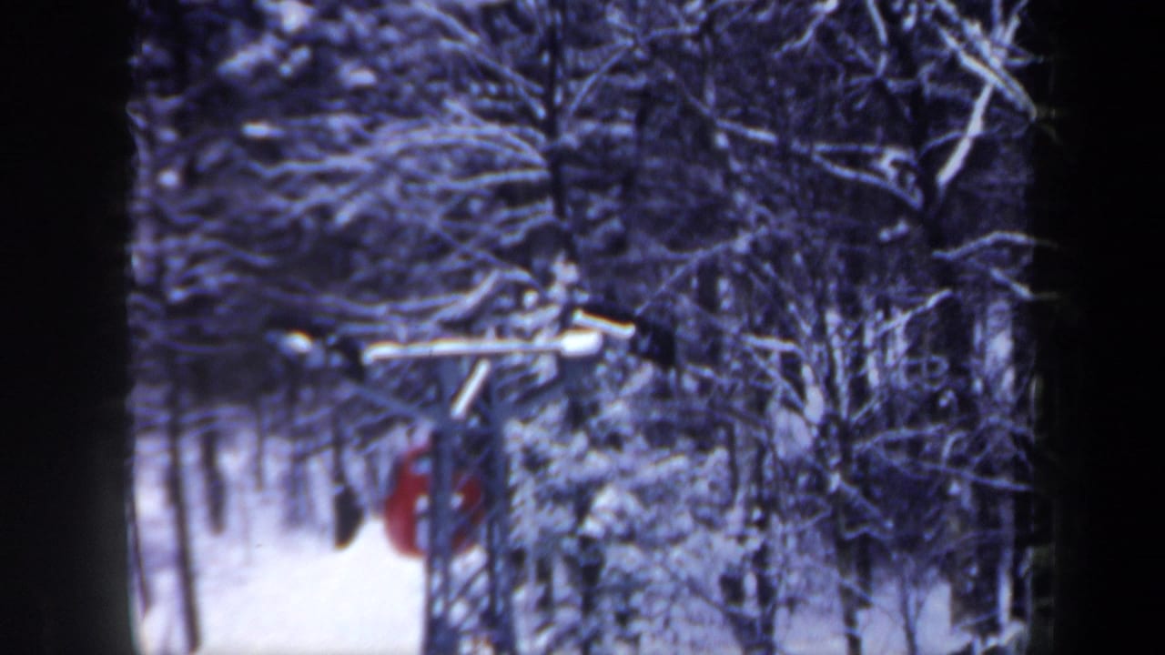 A red ski lift car passes beneath the cable support, surrounded by snow-covered trees in New Hampshire winter footage.