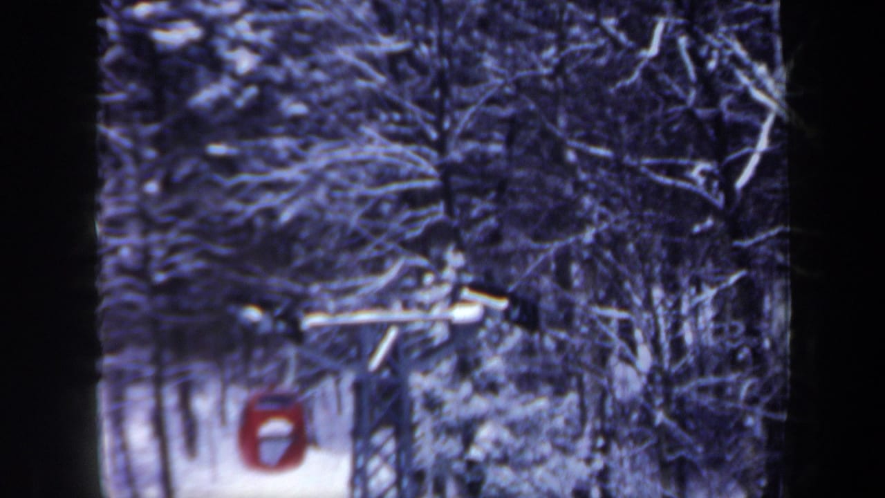 Final frame of the red ski lift car moving through a dense snowy forest, with soft 8mm texture and dark frame edges.