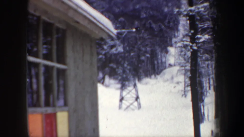 1962 New Hampshire 8mm frame showing a wooden building edge, lift tower, and snow-covered woods at a ski area.