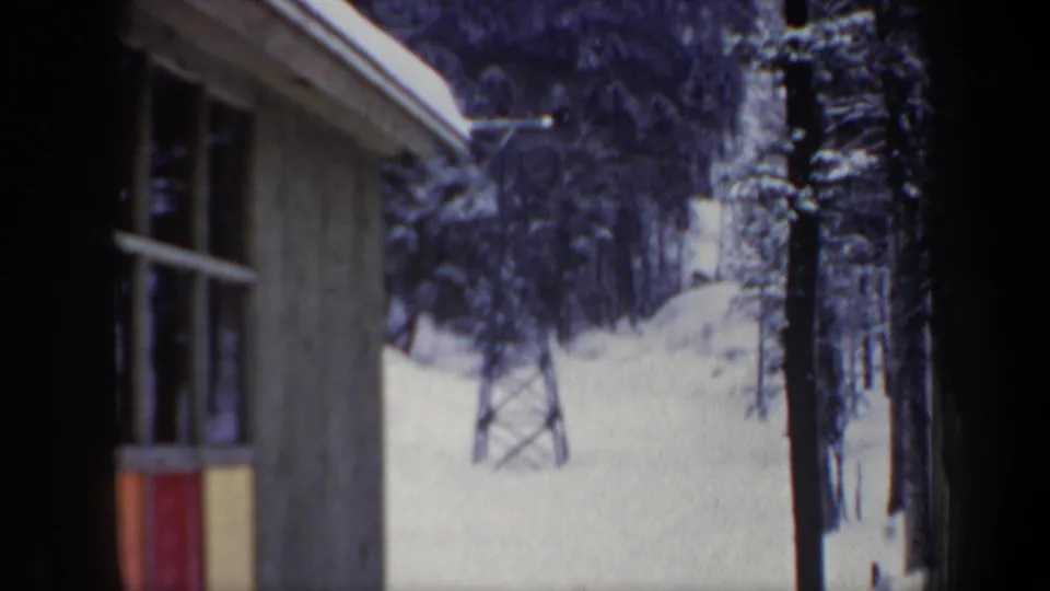 1962 New Hampshire home-movie frame with a wooden ski-area structure, lift tower, and snow-laden trees.