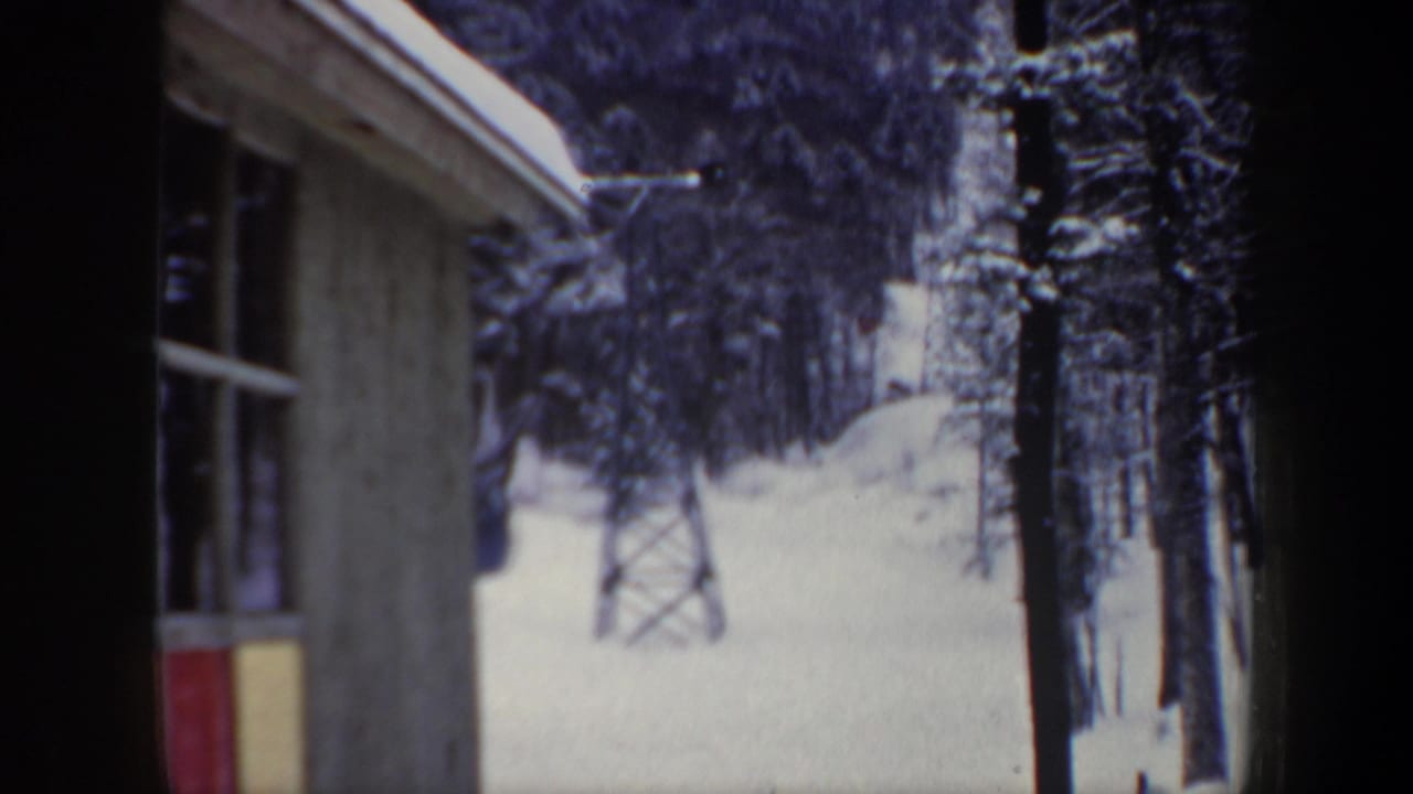 1962 New Hampshire ski-area view from inside a station, with snow, evergreens, and a small lift tower visible outside.