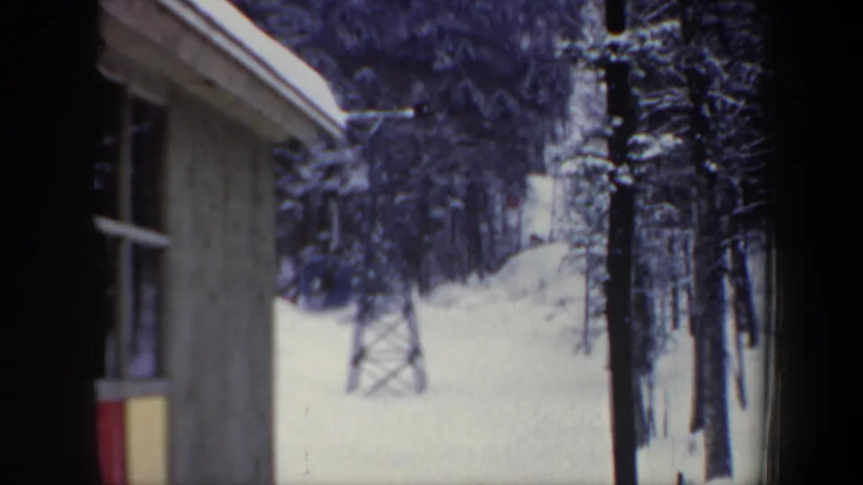 Vintage 8mm New Hampshire ski-area frame showing the station wall, snowfield, trees, and lift support tower.