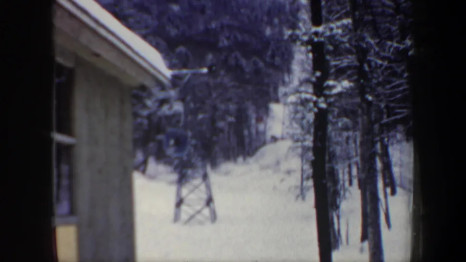 Soft 1962 New Hampshire 8mm frame of a snowy ski lift area, seen past a station post and wall.