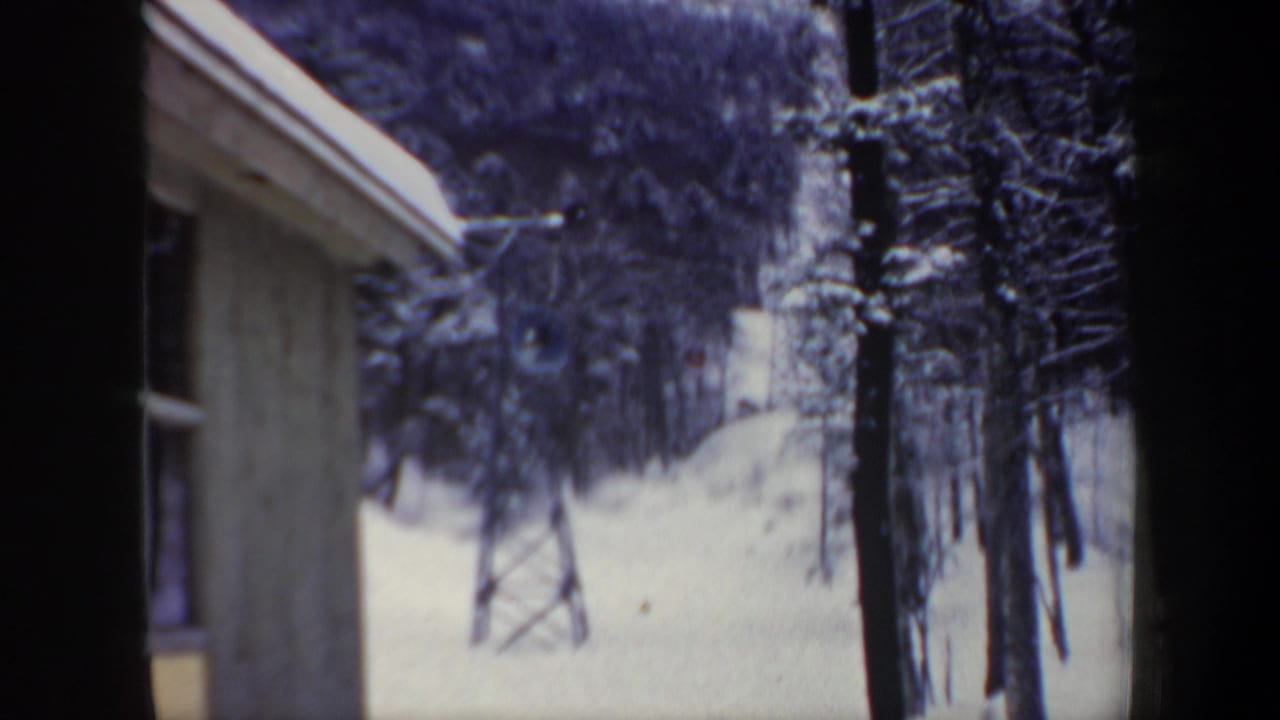 1962 New Hampshire home-movie frame of a snowy ski slope with trees and a lift tower, viewed through a narrow framed opening.
