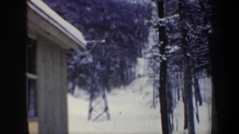 1962 New Hampshire home-movie frame of a snowy ski slope with trees and a lift tower, viewed through a narrow framed opening.