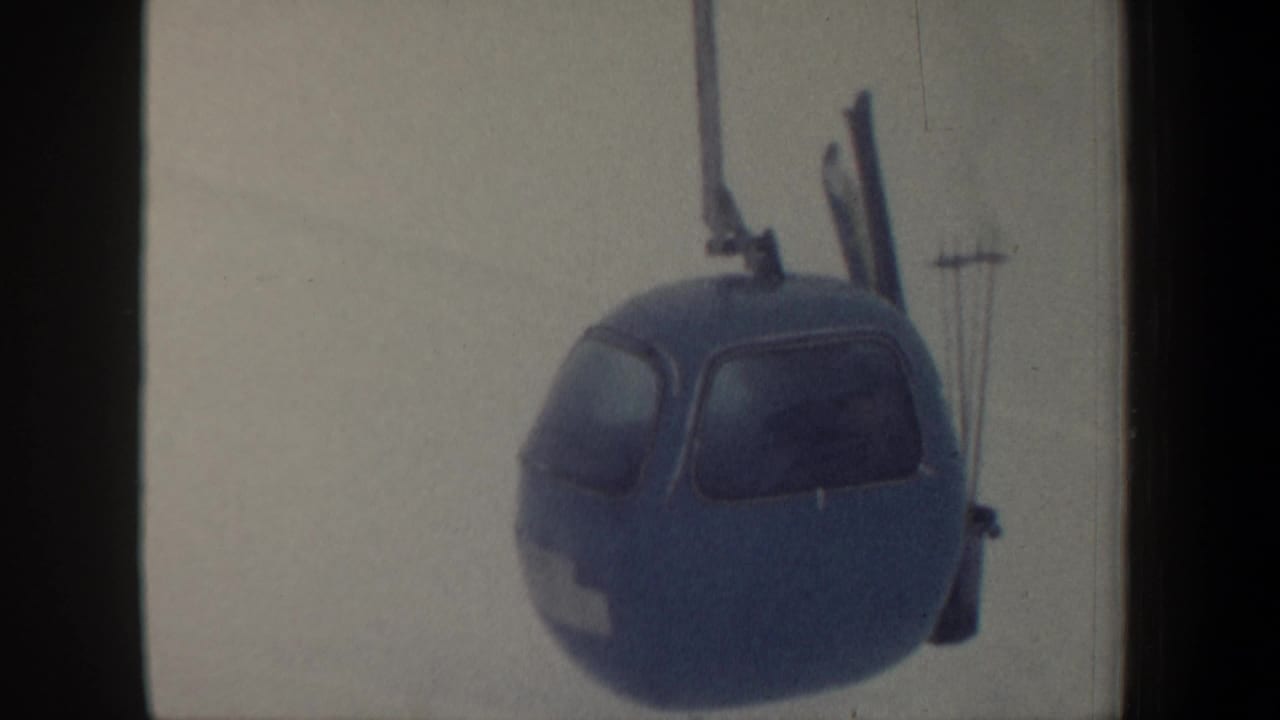 1962 New Hampshire 8mm frame showing a blue gondola lift cabin with exterior skis against a pale snowy mountain backdrop.