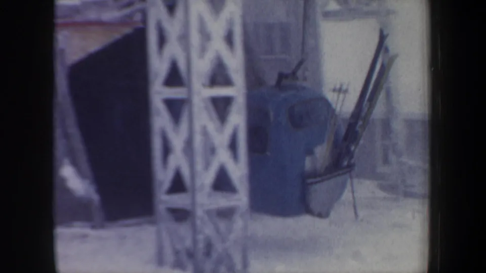 1962 New Hampshire 8mm frame showing the blue gondola cabin near a metal support tower and snowy lift station structure.