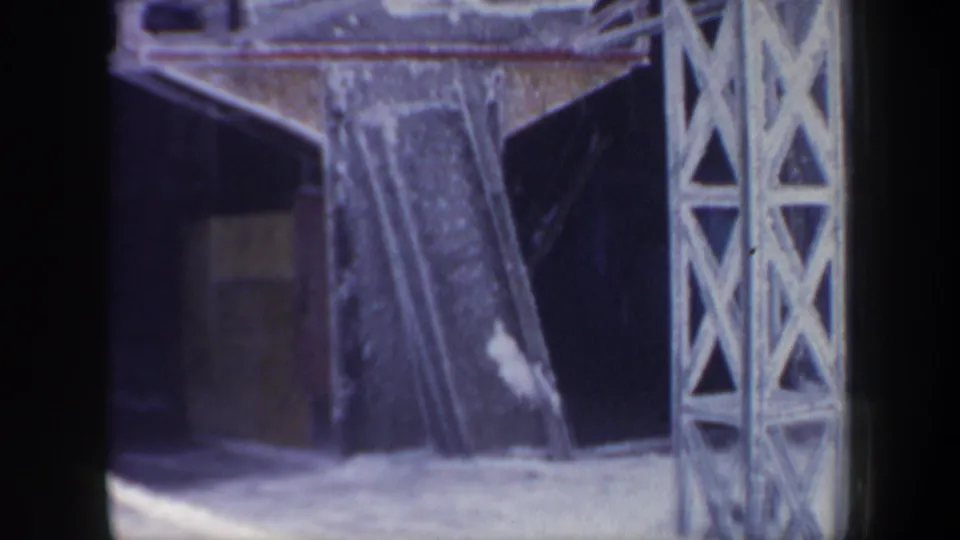 1962 New Hampshire home-movie frame showing the snowy lift station structure and metal tower with the gondola mostly out of view.