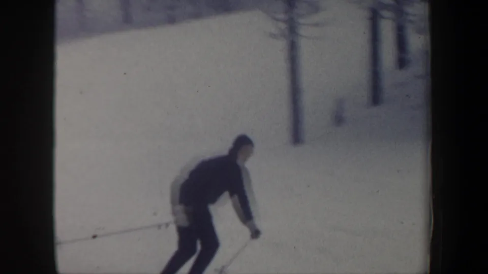 Adult skier in a dark hooded jacket moves across the snow in a 1962 New Hampshire home-movie frame.