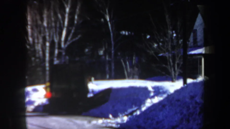 1962 New Hampshire 8mm frame showing a snowy residential exterior at night, with trees, a house edge, and a partial vehicle visible.