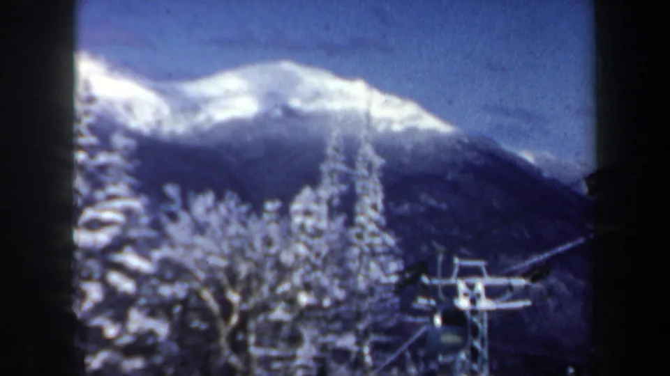 1962 New Hampshire winter frame showing a snow-capped mountain, frosted trees, and a visible ski-lift structure in a home-movie view.