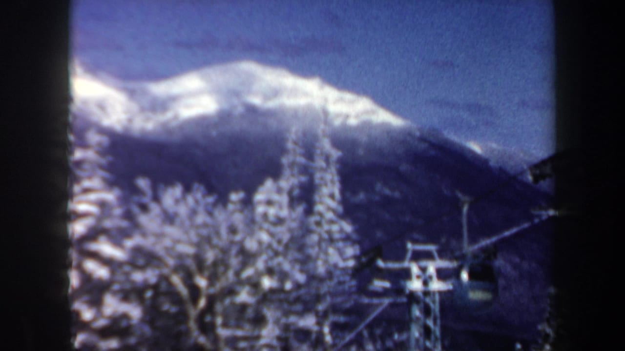 1962 New Hampshire home-movie view of chairlift infrastructure crossing snowy evergreens beneath a clear mountain skyline.