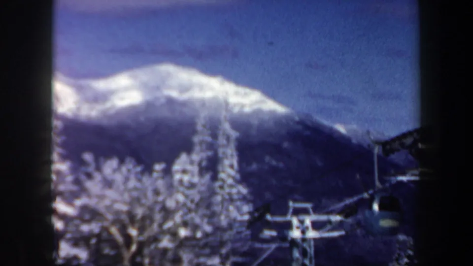 Soft 8mm frame from New Hampshire showing a chairlift beside snowy trees, with a white mountain ridge under blue sky.
