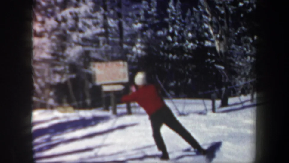 1962 New Hampshire ski-area frame showing a skier in a red jacket moving across snow near evergreens, a posted sign, and lift equipment.