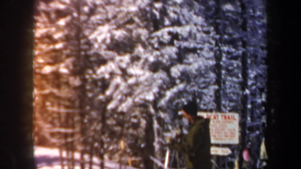 A man in winter clothing appears beside a Wildcat Trail sign among snow-covered trees in New Hampshire footage from 1962.