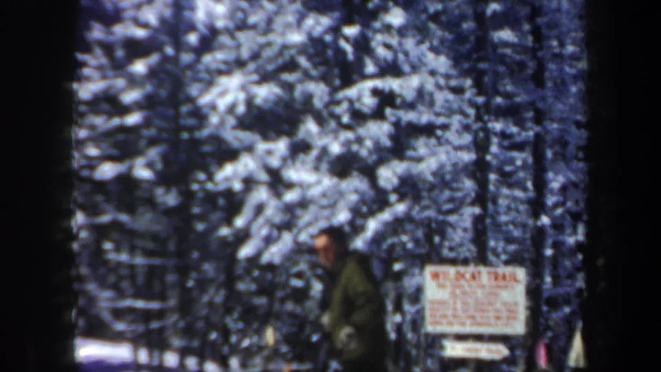 1962 New Hampshire 8mm frame showing a skier near a Wildcat Trail sign among snow-covered evergreen trees.