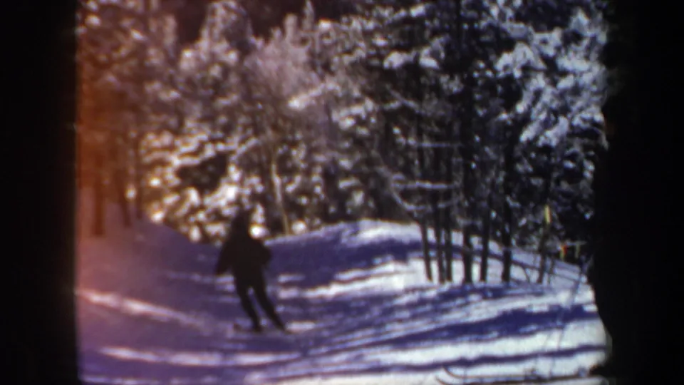 1962 New Hampshire 8mm frame showing a lone skier on a shaded snow trail bordered by evergreen trees.