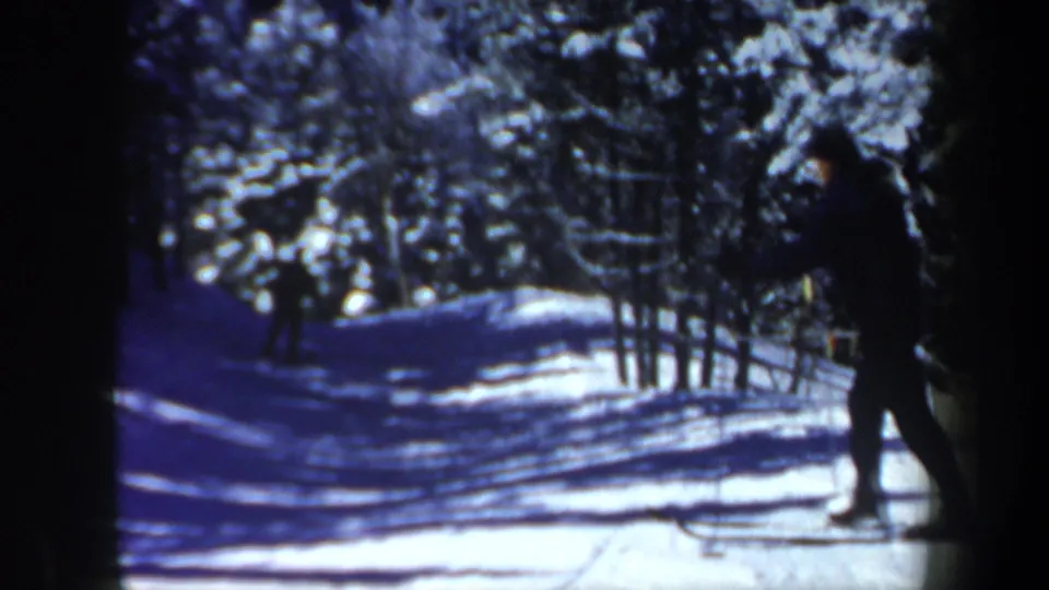1962 New Hampshire 8mm frame showing two adult skiers moving through a snow-covered forest trail.