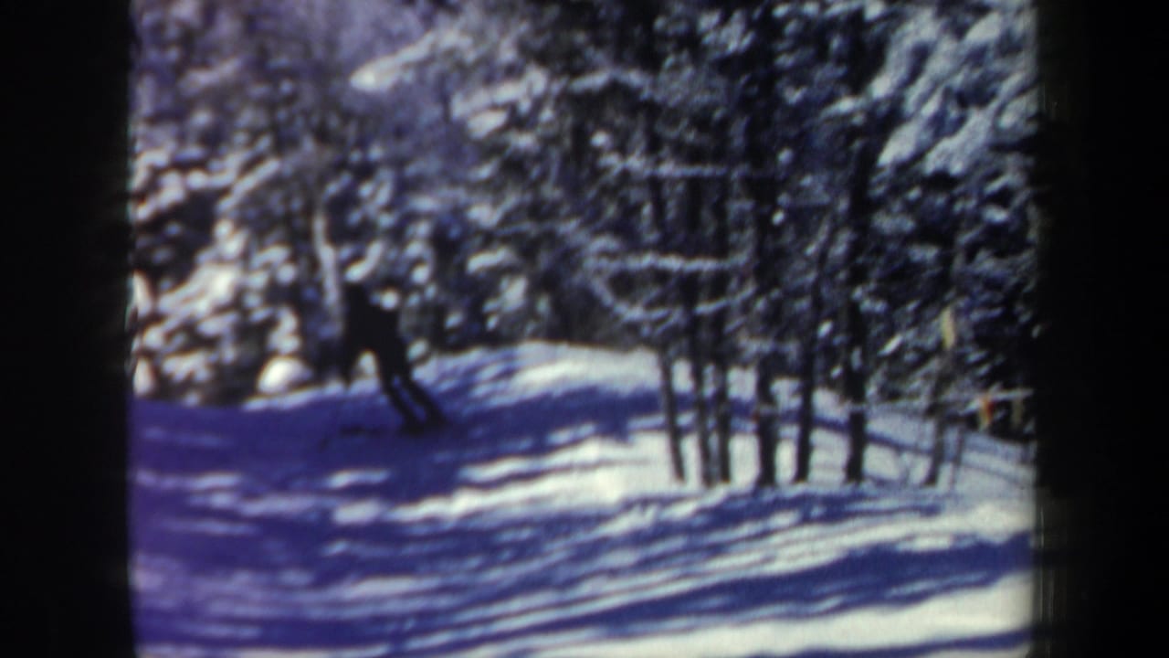 Vintage 8mm frame of a skier silhouetted against snow on a wooded New Hampshire trail.