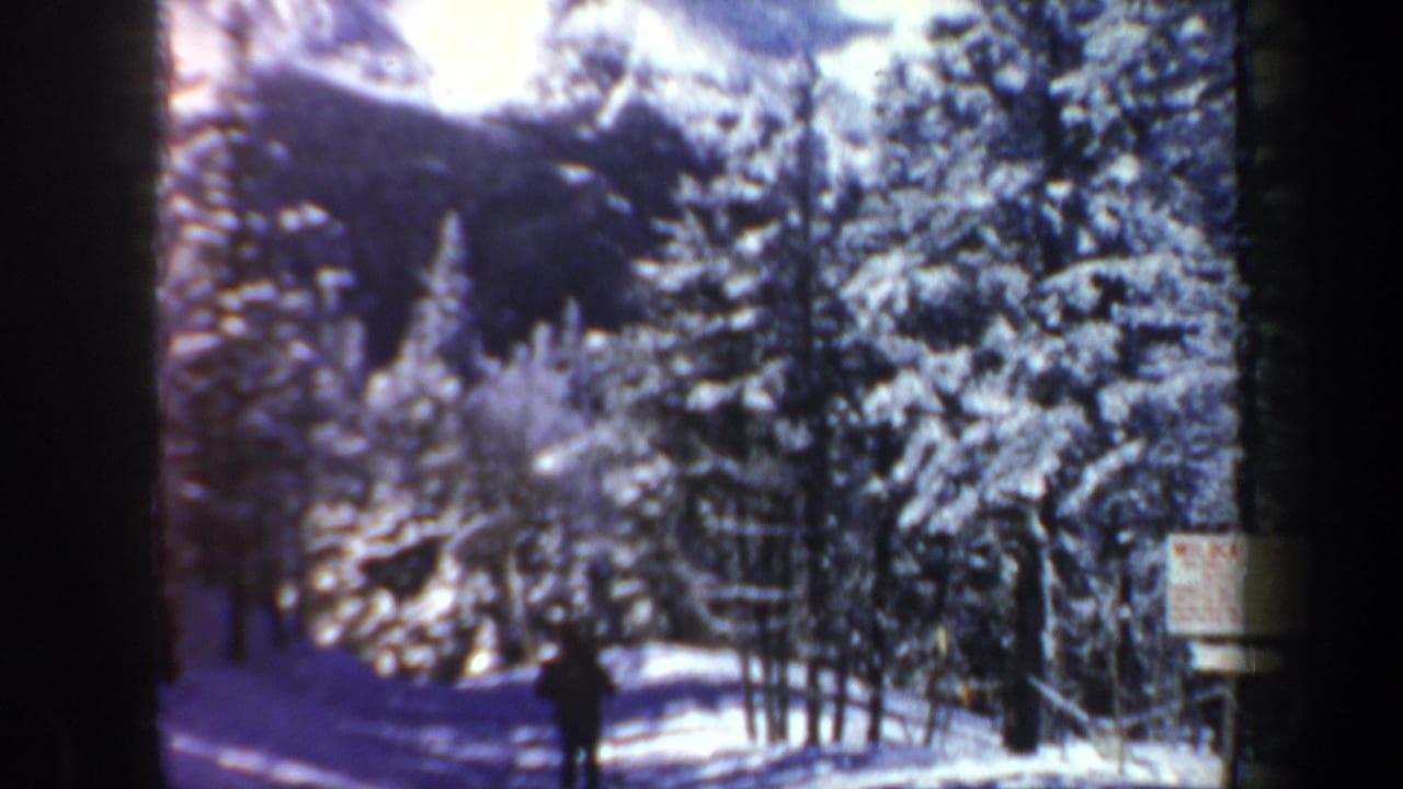 1962 New Hampshire 8mm frame with a distant skier moving through a snowy wooded hillside and a small posted sign nearby.