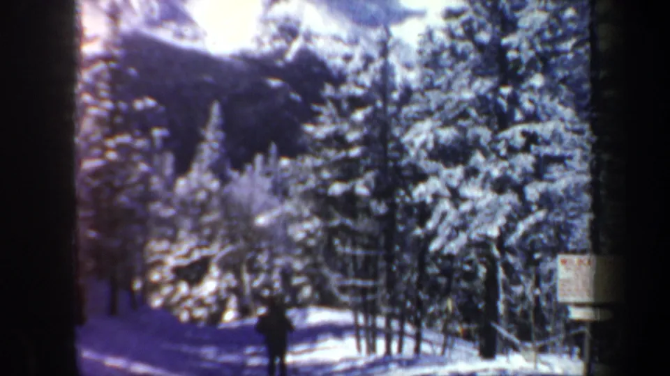 1962 New Hampshire 8mm frame with a distant skier moving through a snowy wooded hillside and a small posted sign nearby.