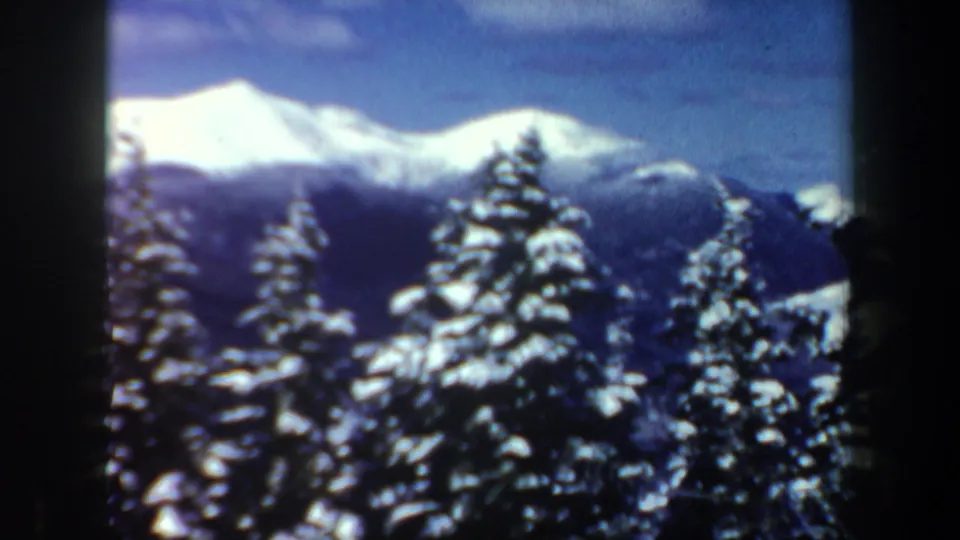 Wide 1962 New Hampshire 8mm view of snowy evergreens and distant mountain peaks after the skier shot.
