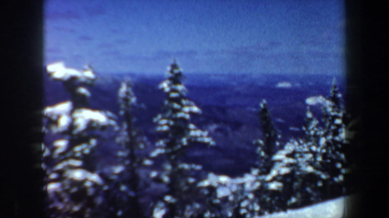 1962 New Hampshire 8mm frame with snow-laden conifers, a blue mountain horizon, and visible home-movie frame borders.