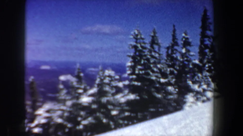 1962 New Hampshire 8mm frame with snow-covered evergreen treetops, a bright white slope, and distant blue mountain layers.
