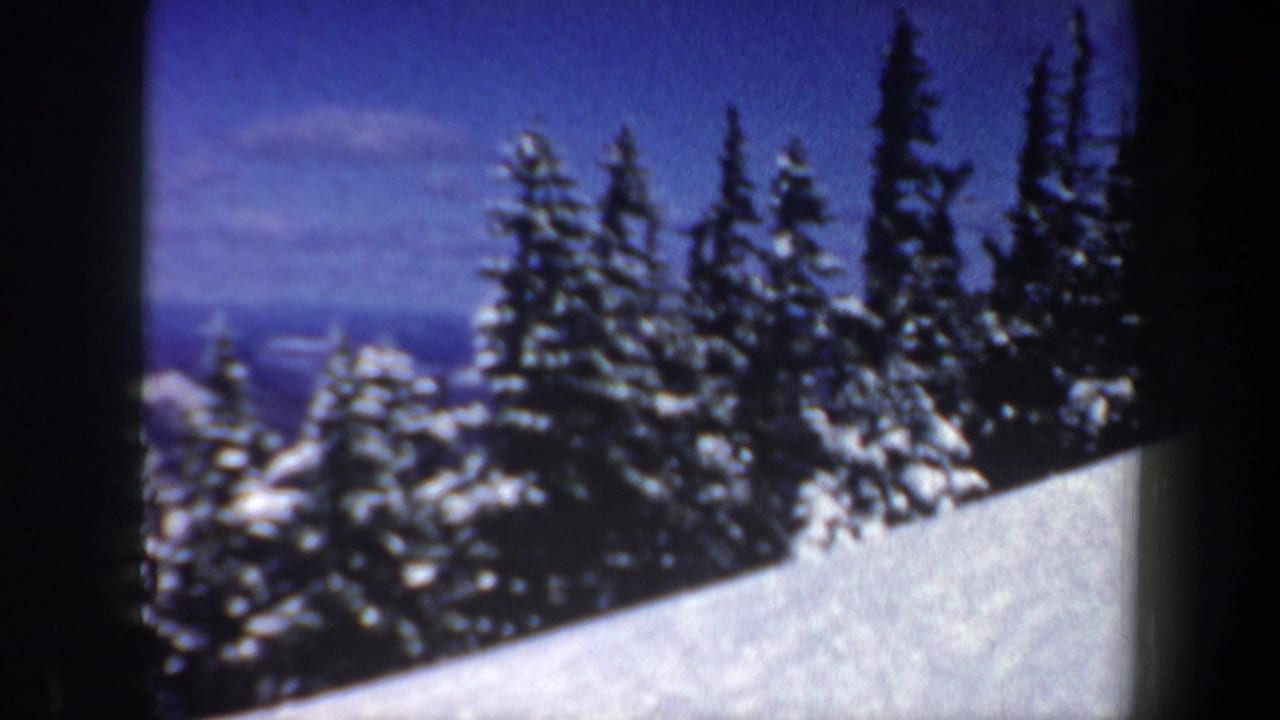 1962 New Hampshire 8mm frame showing a snowy slope bordered by dark evergreen trees beneath a blue winter sky.