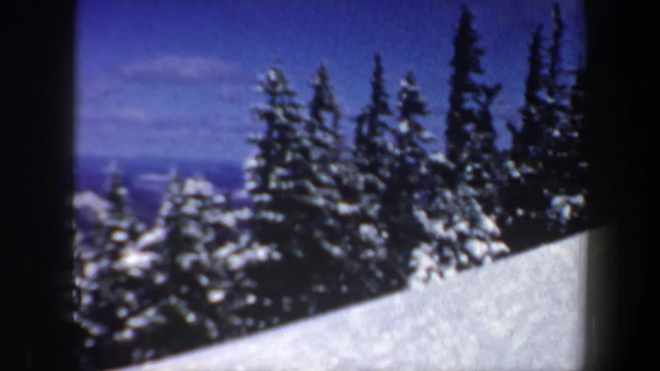 1962 New Hampshire 8mm frame showing a snowy slope bordered by dark evergreen trees beneath a blue winter sky.