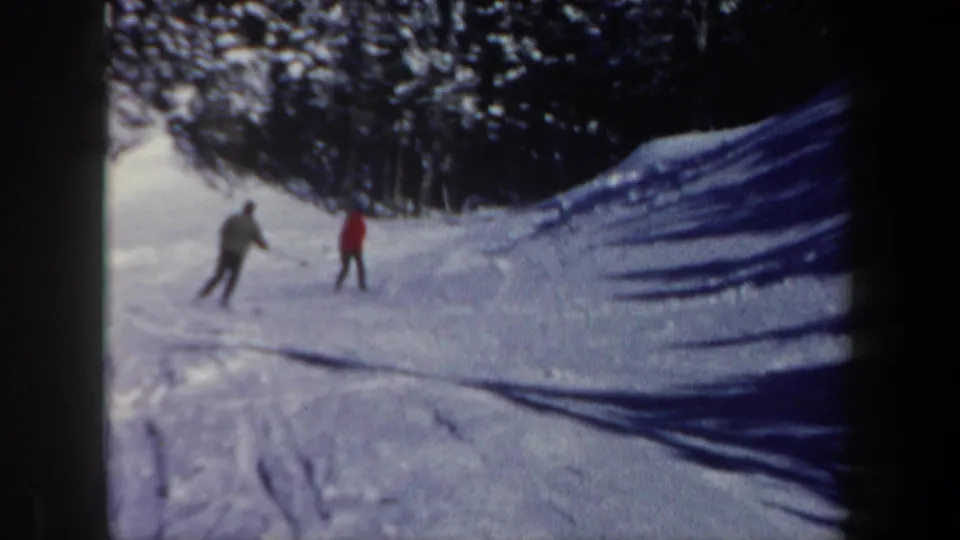 Two distant skiers, one in a red jacket and one in darker clothing, appear on a snowy New Hampshire slope in 1962 footage.