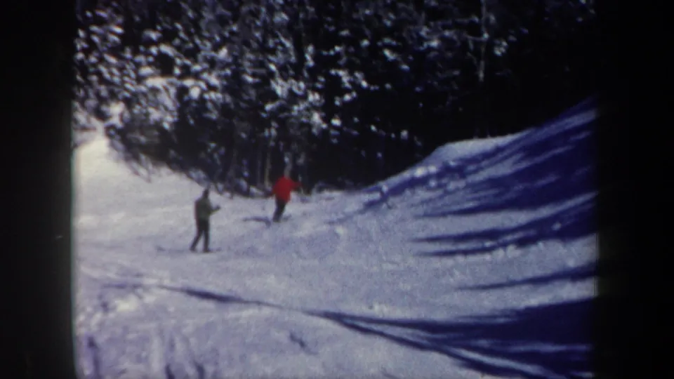 The pair of skiers continues downhill across a snowy New Hampshire run, framed by trees and blue-toned shadows.