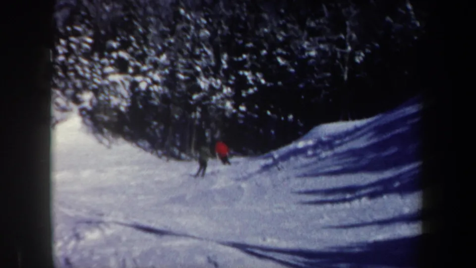 A distant skier in a red jacket appears to turn or crouch on the snowy New Hampshire slope as another figure remains nearby.