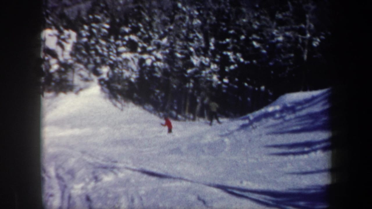 1962 New Hampshire 8mm frame showing a distant red-clad skier moving across a snowy forested slope.