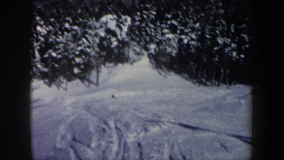 1962 New Hampshire 8mm frame showing a snowy slope, evergreen backdrop, and a small distant dark figure or object.