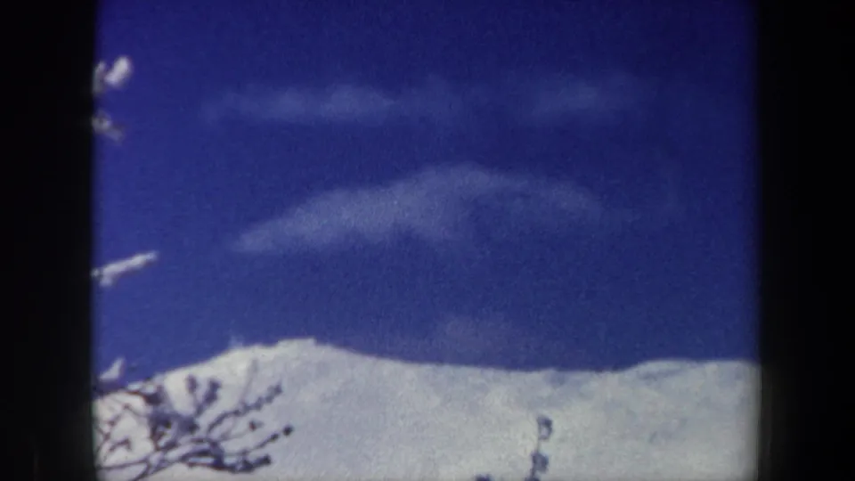 1962 New Hampshire 8mm frame looking toward blue sky, scattered clouds, and a bright snow-covered ridge.