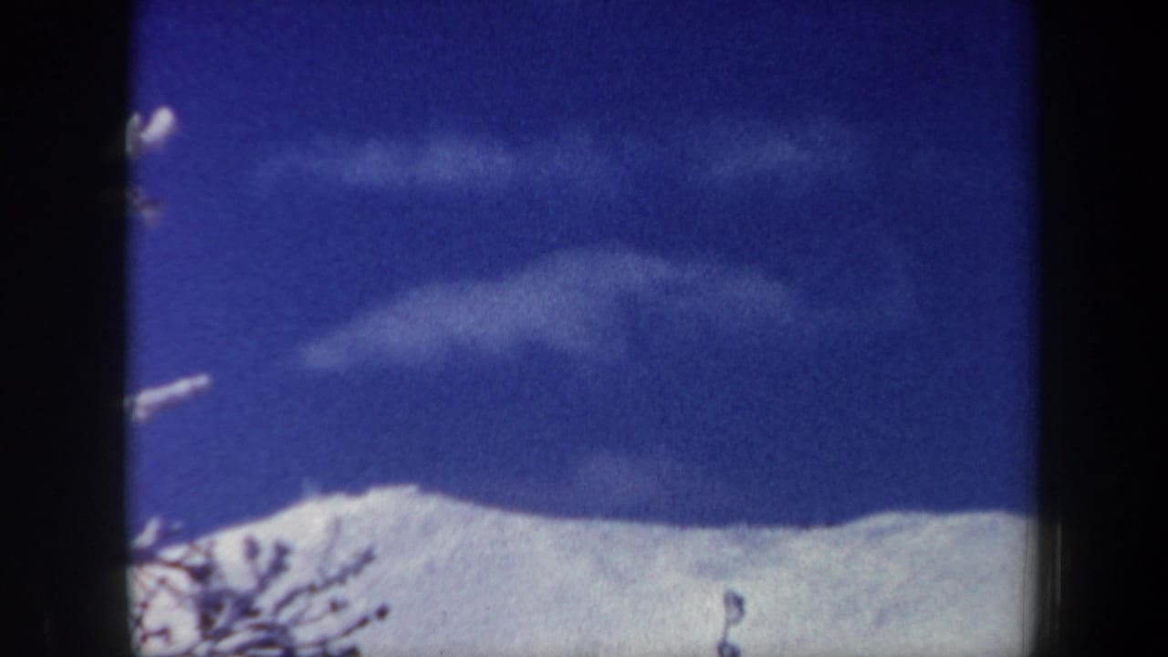 1962 New Hampshire home-movie frame showing a snow-covered ridge under a deep blue sky with wispy clouds and bare branches.