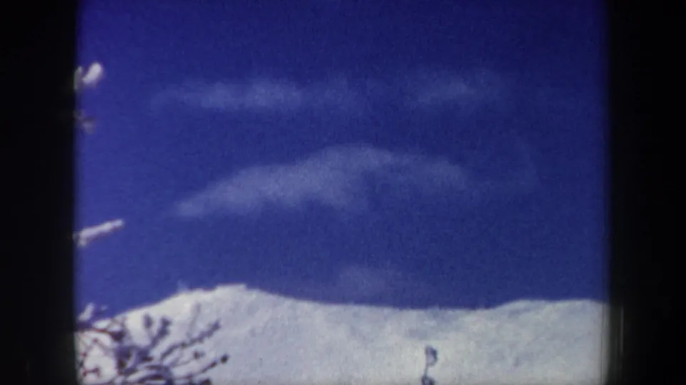 1962 New Hampshire home-movie frame showing a snow-covered ridge under a deep blue sky with wispy clouds and bare branches.