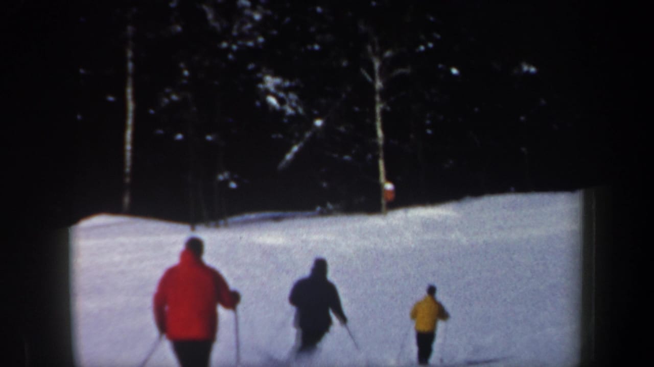 Three skiers in red, dark, and yellow jackets move downhill on a snowy New Hampshire slope in 1962 home-movie footage.