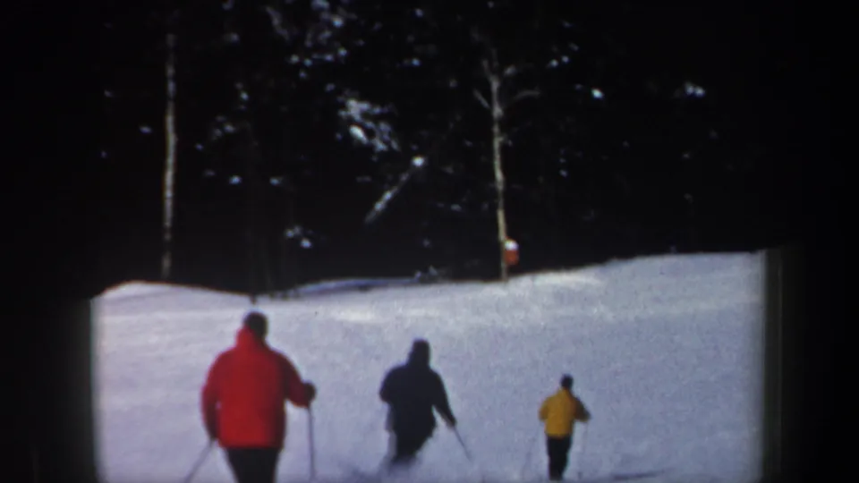 Three skiers in red, dark, and yellow jackets move downhill on a snowy New Hampshire slope in 1962 home-movie footage.