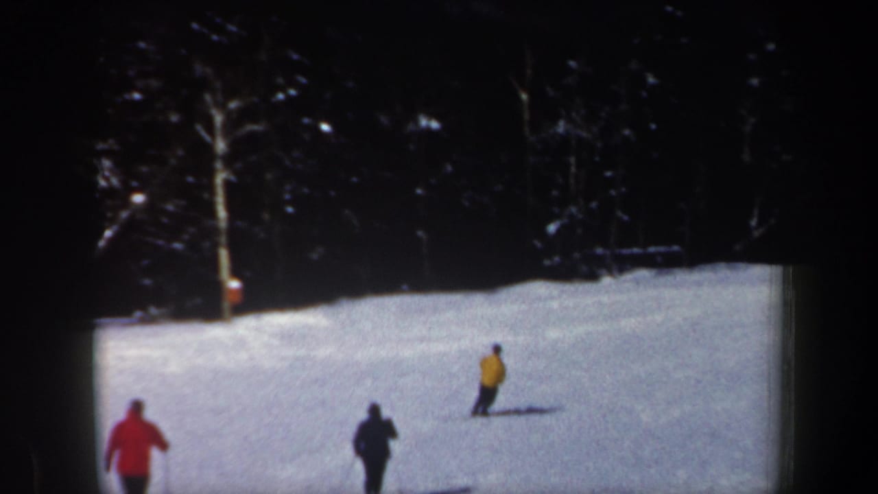 Three distant skiers cross a bright snowy slope near a wooded edge.
